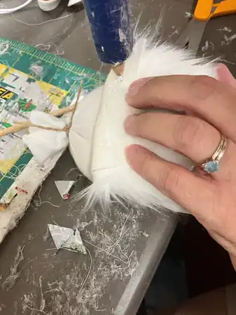 Hands adding tiny flower and lace details to a gnome with a low-temperature glue gun